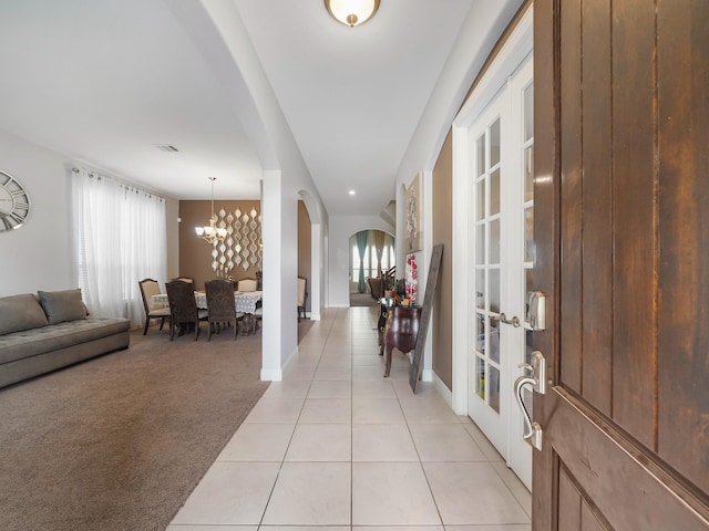 foyer entrance featuring light tile patterned floors, french doors, a notable chandelier, arched walkways, and light carpet