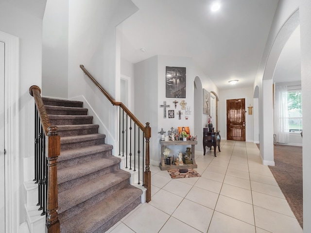 foyer featuring light tile patterned floors, stairway, baseboards, and arched walkways