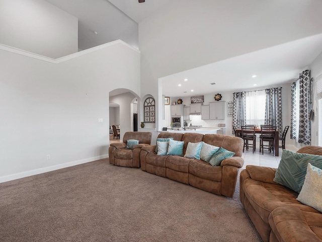 living area with light colored carpet, a high ceiling, baseboards, and arched walkways