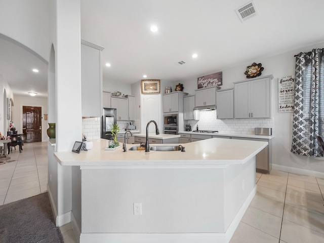 kitchen with a sink, backsplash, arched walkways, light tile patterned floors, and appliances with stainless steel finishes