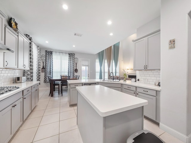 kitchen with a sink, a peninsula, stainless steel gas stovetop, visible vents, and decorative backsplash