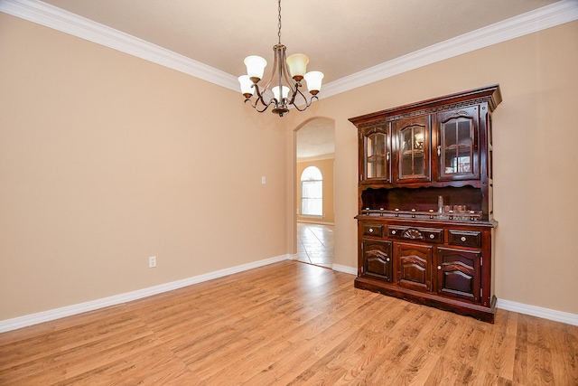spare room featuring light wood finished floors, an inviting chandelier, crown molding, baseboards, and arched walkways