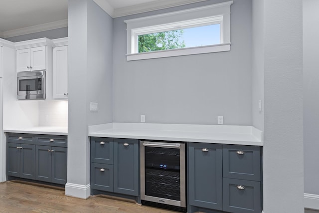 bar with stainless steel microwave, tasteful backsplash, crown molding, beverage cooler, and light wood-style floors