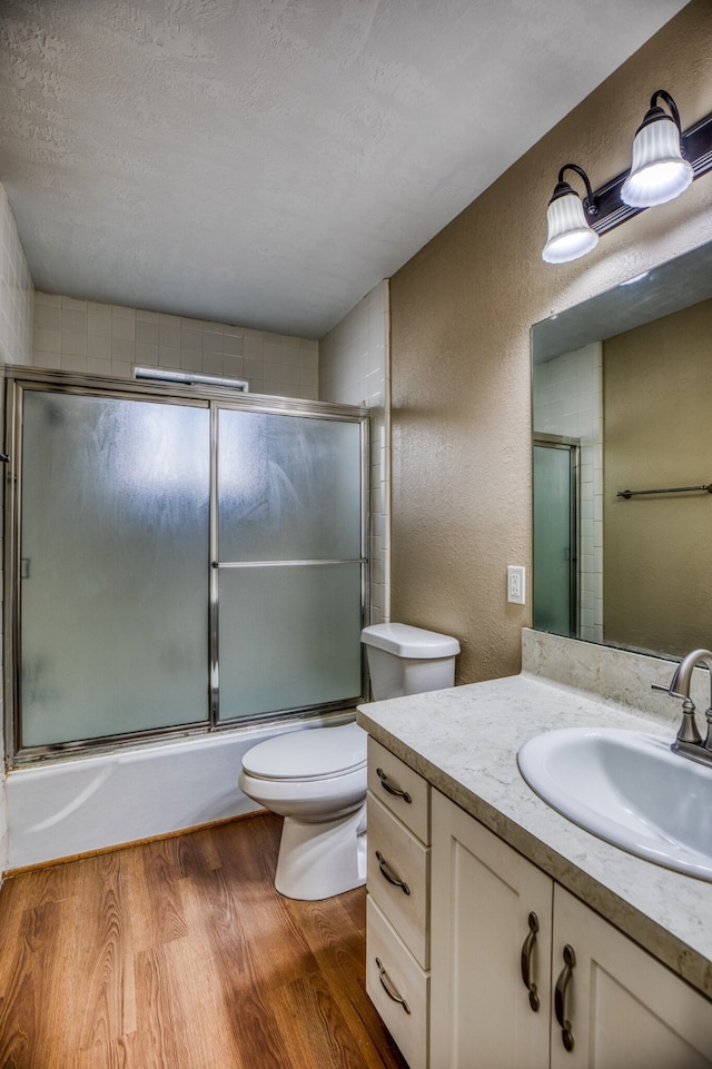 401 E Main St, Brenham, TX 77833 - bathroom with wood finished floors, bath / shower combo with glass door, toilet, vanity, and a textured wall