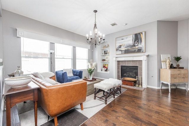 living room featuring wood finished floors, visible vents, built in shelves, a chandelier, and a tiled fireplace