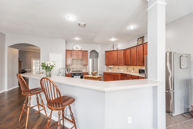 kitchen with brown cabinetry, a breakfast bar, stainless steel appliances, and decorative backsplash