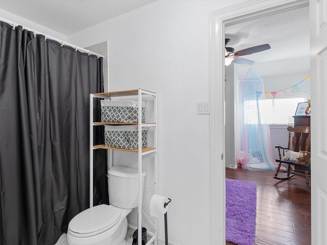 bathroom featuring toilet, wood finished floors, a shower with curtain, ceiling fan, and a textured wall