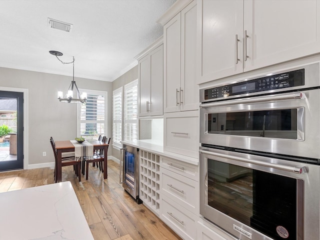 kitchen with ornamental molding, light wood-type flooring, double oven, a chandelier, and baseboards