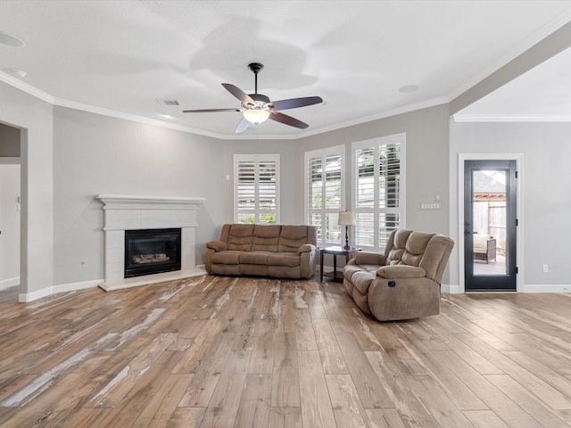 living area featuring ceiling fan, crown molding, a glass covered fireplace, and light wood-style floors