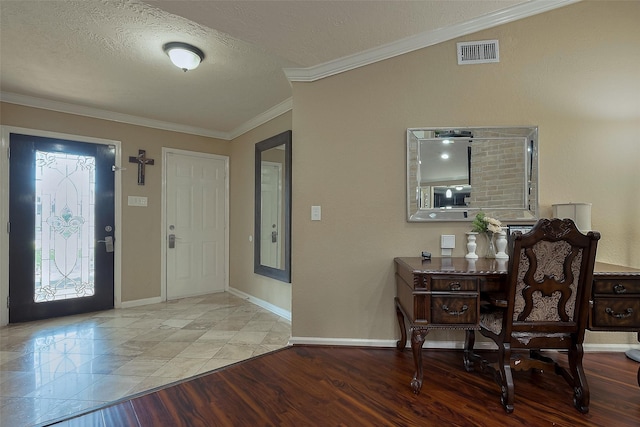 foyer entrance featuring a textured ceiling, baseboards, visible vents, crown molding, and wood finished floors