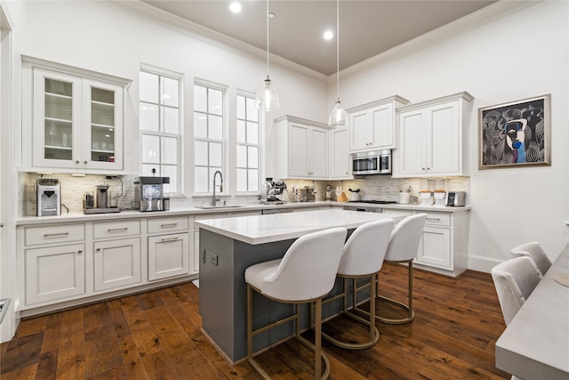 kitchen featuring stainless steel microwave, a sink, tasteful backsplash, crown molding, and a center island
