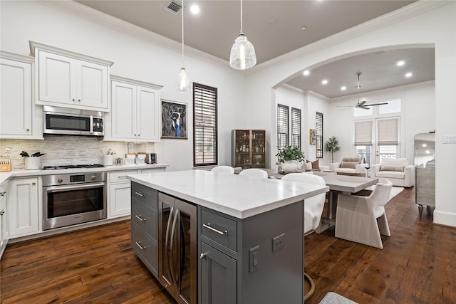 kitchen with stainless steel appliances, wine cooler, ornamental molding, visible vents, and arched walkways