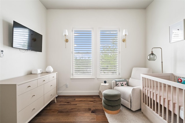 bedroom with baseboards, dark wood-style flooring, and a crib