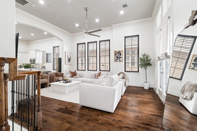 living room featuring dark wood-type flooring, visible vents, crown molding, ceiling fan, and arched walkways