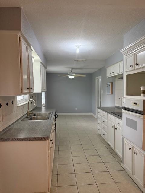 1101 E Brown Ln, Deer Park, TX 77536 - kitchen with a sink, dark countertops, ceiling fan, white oven, and light tile patterned flooring