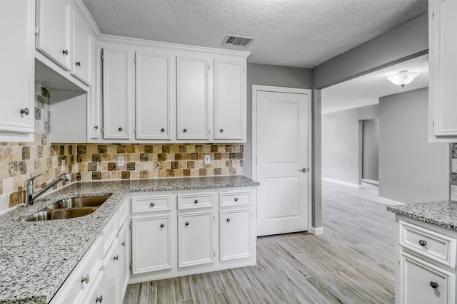 kitchen with light stone countertops, visible vents, a sink, white cabinetry, and decorative backsplash