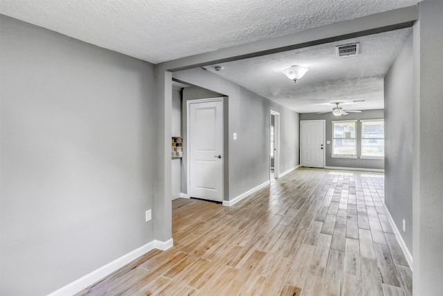 empty room featuring a textured ceiling, light wood-type flooring, visible vents, a ceiling fan, and baseboards