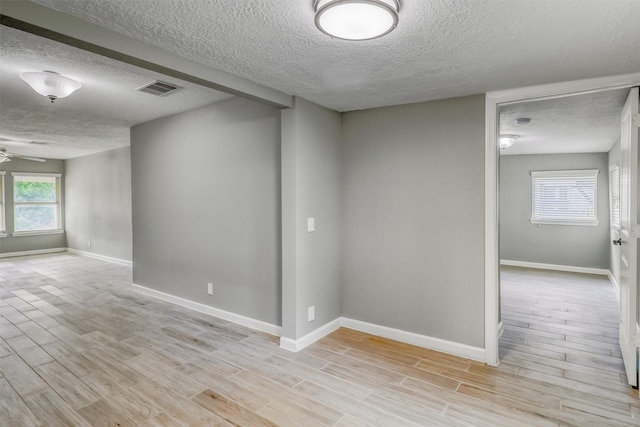 unfurnished room featuring a textured ceiling, visible vents, baseboards, and light wood-style floors