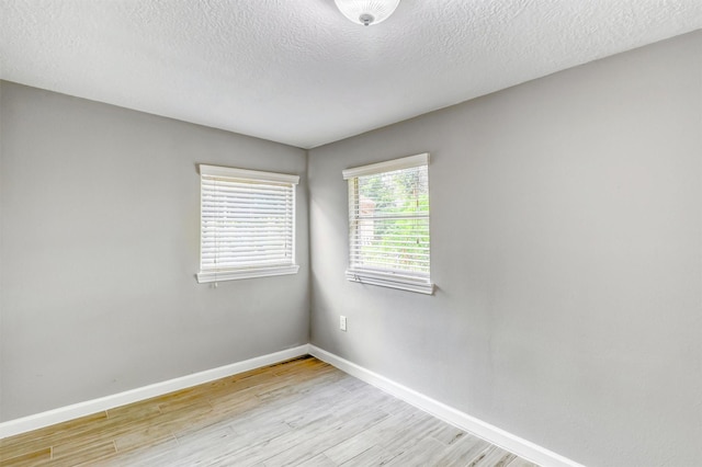 spare room featuring baseboards, light wood-style flooring, and a textured ceiling