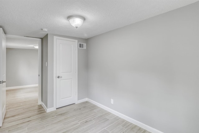 spare room featuring baseboards, light wood-style flooring, visible vents, and a textured ceiling
