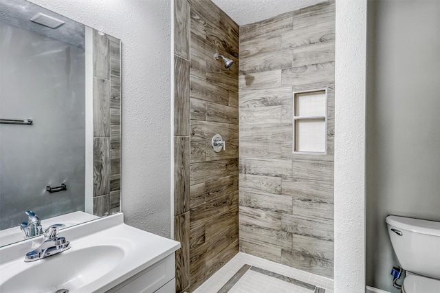 bathroom with vanity, toilet, and tiled shower
