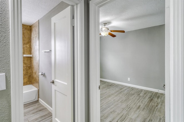 full bathroom with a textured ceiling, baseboards, a ceiling fan, and wood finished floors