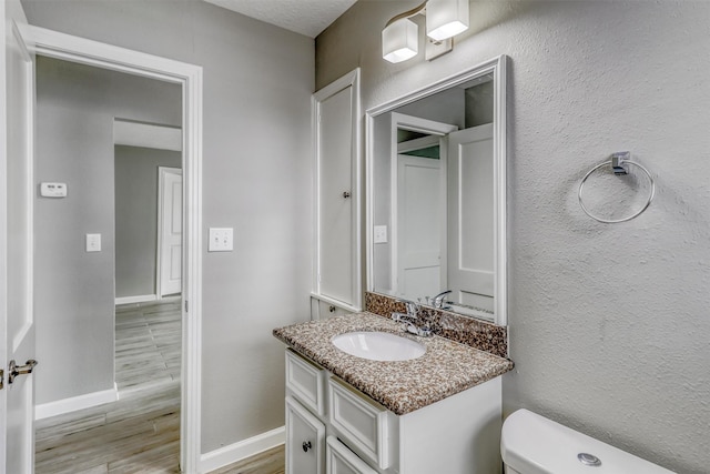 half bath with toilet, baseboards, vanity, and wood finished floors