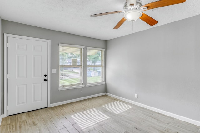 empty room featuring a textured ceiling, baseboards, a ceiling fan, and light wood-style floors