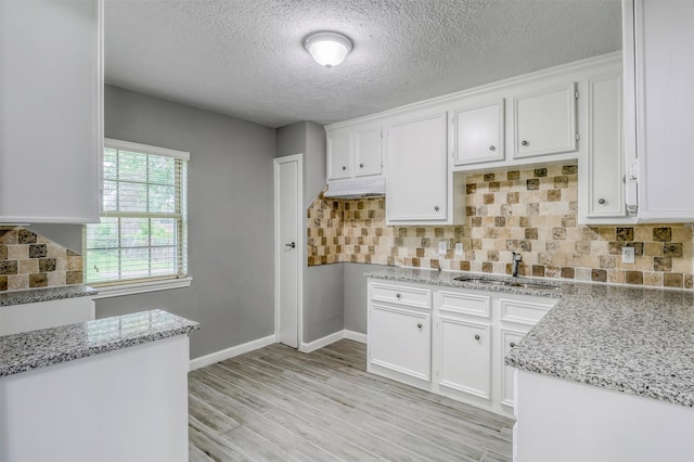 kitchen with a textured ceiling, white cabinetry, light stone countertops, and a sink