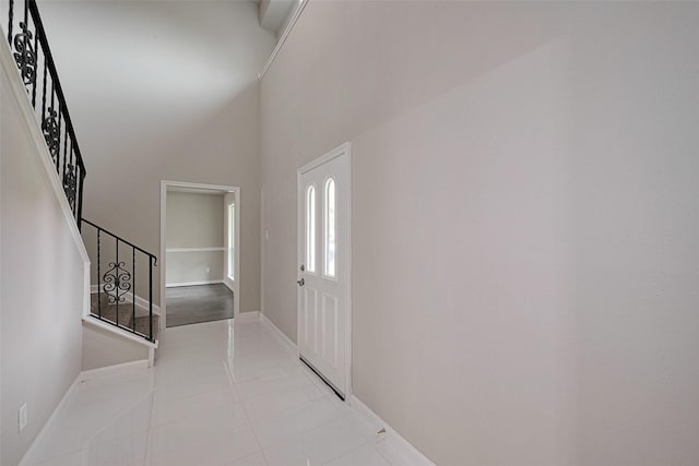 foyer with light tile patterned floors, stairway, baseboards, and a towering ceiling