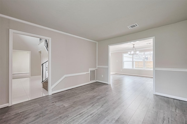 spare room featuring baseboards, a chandelier, visible vents, and wood finished floors