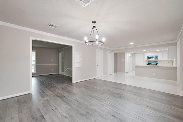 unfurnished living room featuring ornamental molding, light wood-type flooring, visible vents, an inviting chandelier, and baseboards