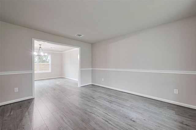 unfurnished room with visible vents, wood finished floors, baseboards, and a notable chandelier