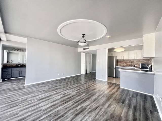 unfurnished living room featuring a sink, wood finished floors, visible vents, recessed lighting, and baseboards