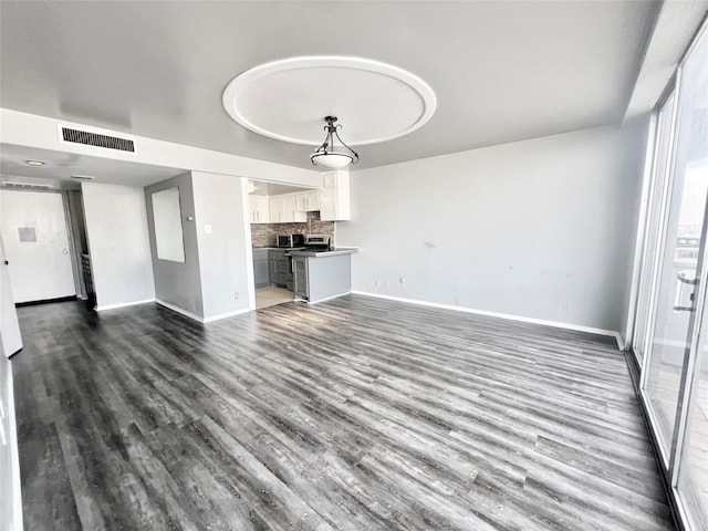 unfurnished living room featuring visible vents, wood finished floors, and baseboards