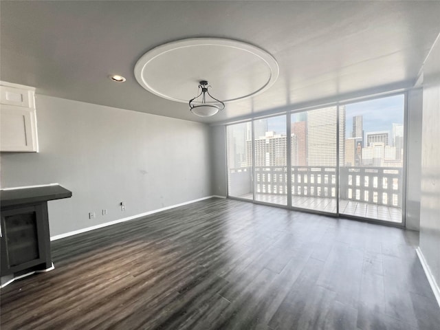 unfurnished living room with recessed lighting, baseboards, a wall of windows, a city view, and dark wood-type flooring