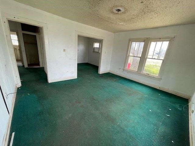 unfurnished bedroom featuring baseboards, multiple windows, a textured ceiling, and carpet floors