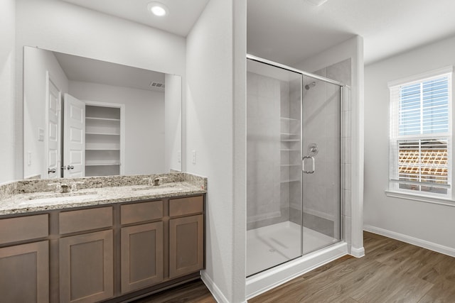 bathroom with a stall shower, double vanity, a sink, and wood finished floors