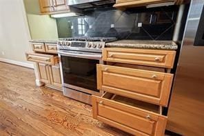 details featuring stainless steel range with gas cooktop, backsplash, baseboards, and wood finished floors