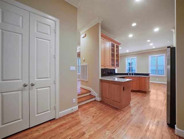 kitchen with a peninsula, freestanding refrigerator, visible vents, baseboards, and ornamental molding
