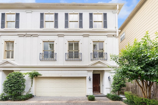 view of front of home featuring a balcony, an attached garage, fence, and decorative driveway