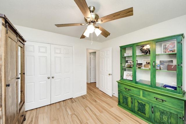 11202 Leah Elizabeth Dr, Needville, TX 77461 - unfurnished bedroom with light wood-type flooring, a ceiling fan, baseboards, a closet, and a barn door