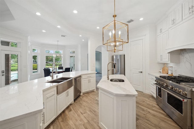 kitchen featuring a sink, high end appliances, visible vents, and a center island with sink