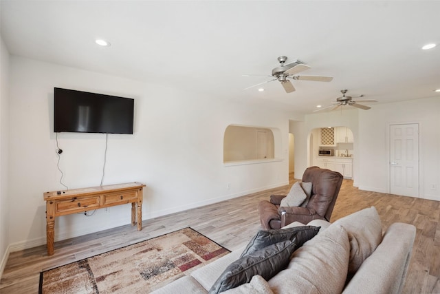 living area with light wood-type flooring, a ceiling fan, arched walkways, and recessed lighting