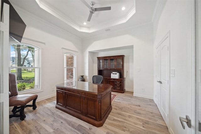 office space with a ceiling fan, ornamental molding, light wood finished floors, and a tray ceiling