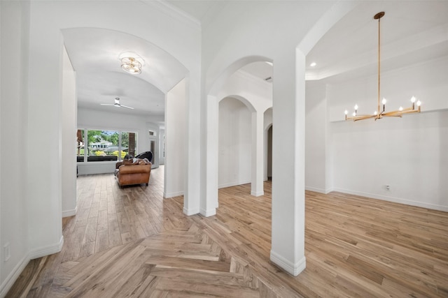 interior space featuring baseboards, ceiling fan with notable chandelier, crown molding, wood finished floors, and arched walkways