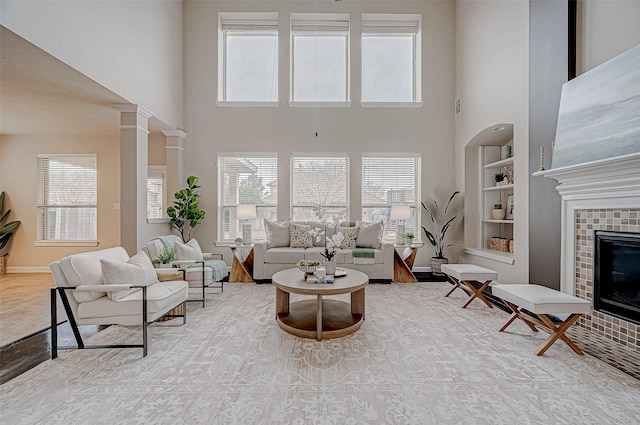 living room featuring a tile fireplace, plenty of natural light, a high ceiling, and built in shelves