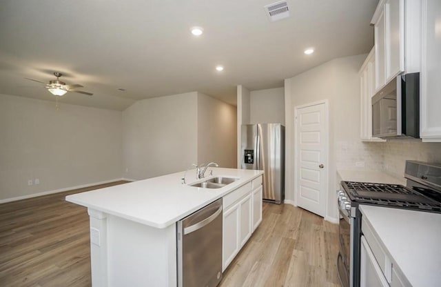 kitchen featuring light wood finished floors, a sink, a center island with sink, backsplash, and appliances with stainless steel finishes