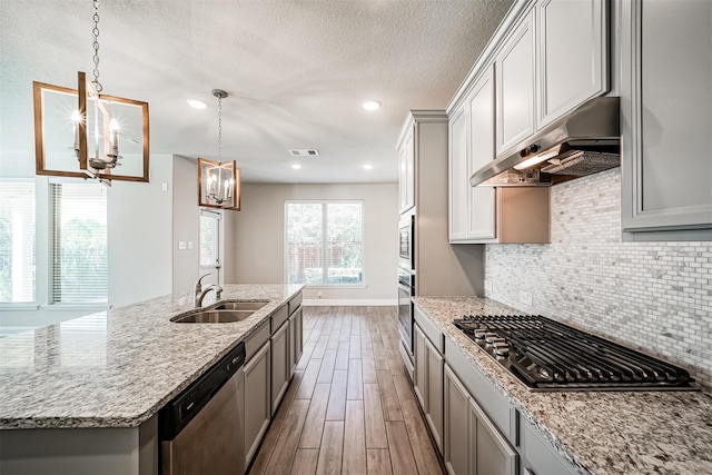 kitchen featuring wood finished floors, a sink, stainless steel appliances, under cabinet range hood, and a chandelier
