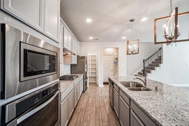 kitchen featuring hanging light fixtures, an inviting chandelier, a sink, light wood-style floors, and stainless steel appliances